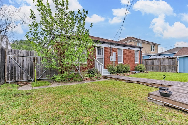 back of property featuring fence, a wooden deck, entry steps, brick siding, and a yard