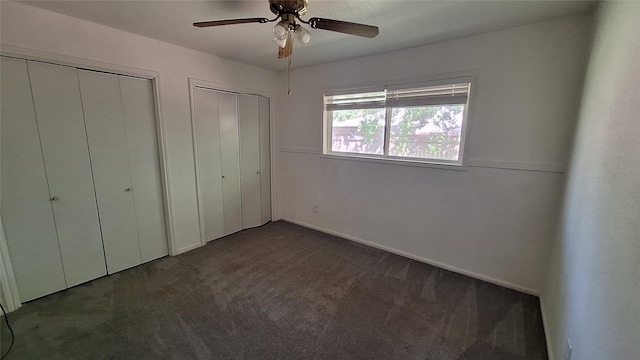 unfurnished bedroom with baseboards, dark carpet, ceiling fan, and multiple closets