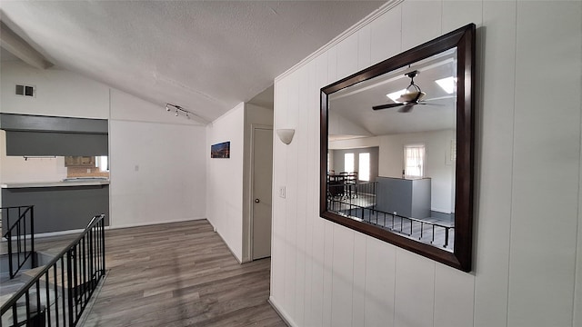 hallway with visible vents, wood finished floors, an upstairs landing, and vaulted ceiling