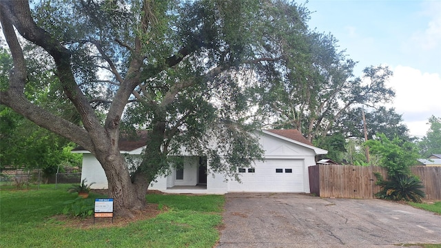 view of property hidden behind natural elements featuring a front yard, driveway, an attached garage, and fence