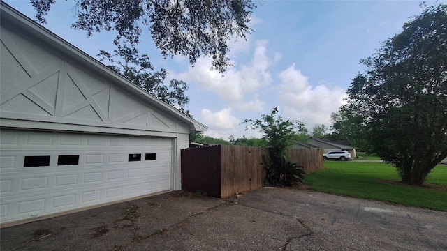 view of home's exterior featuring fence, aphalt driveway, an outbuilding, a garage, and a lawn