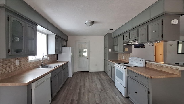 kitchen with gray cabinetry, white appliances, backsplash, and a sink