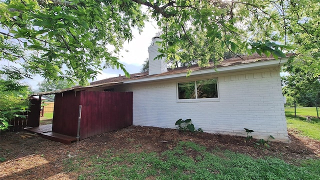 view of home's exterior featuring fence, a chimney, and brick siding