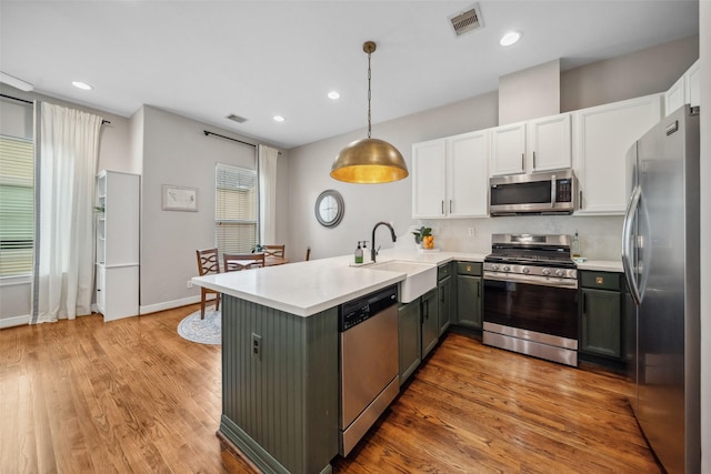 kitchen with a peninsula, a sink, white cabinets, visible vents, and appliances with stainless steel finishes