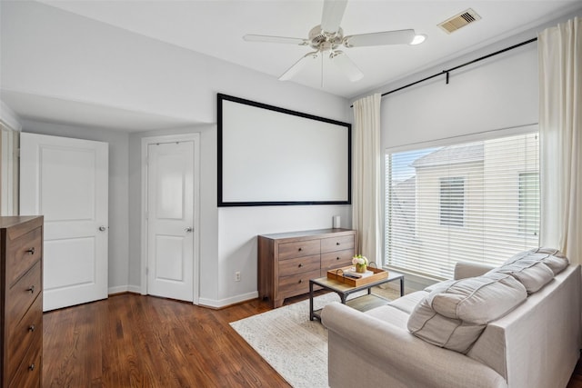 home theater featuring visible vents, baseboards, a ceiling fan, and dark wood-style floors