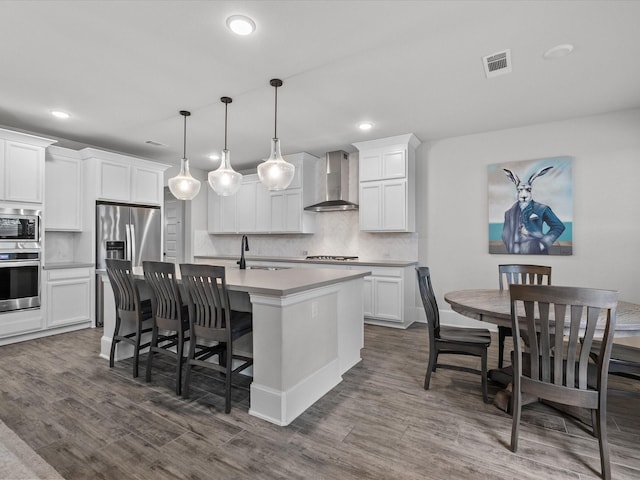 2712 Ahnya Ln, League City, TX 77573 - kitchen featuring wall chimney exhaust hood, tasteful backsplash, appliances with stainless steel finishes, a kitchen island with sink, and dark wood-type flooring