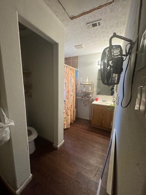 7511 Bonham St, Houston, TX 77020 - full bathroom featuring wood finished floors, vanity, toilet, a shower with shower curtain, and a textured ceiling
