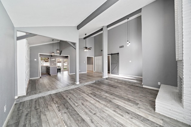 unfurnished living room with visible vents, baseboards, ceiling fan, wood finished floors, and a barn door