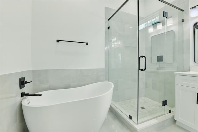 bathroom with tile walls, vanity, a stall shower, a freestanding bath, and wainscoting