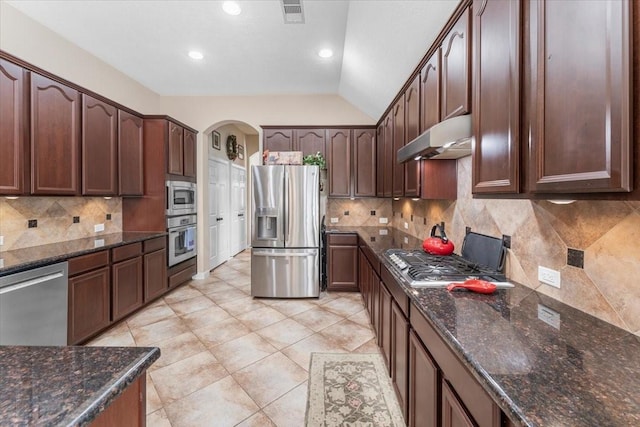 2052 Doolan Dr, Conroe, TX 77301 - kitchen with appliances with stainless steel finishes, under cabinet range hood, lofted ceiling, decorative backsplash, and arched walkways