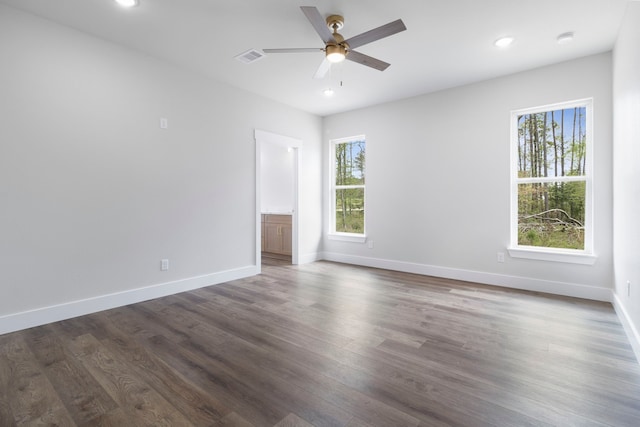 empty room featuring dark wood-style flooring, a ceiling fan, and a healthy amount of sunlight