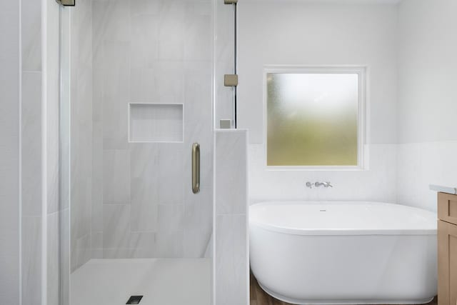 full bath with a soaking tub, vanity, a stall shower, and tile walls