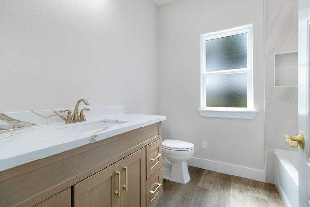 bathroom featuring baseboards, toilet, wood finished floors, vanity, and a tub to relax in