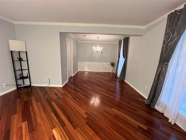 empty room featuring a chandelier, baseboards, crown molding, and wood finished floors
