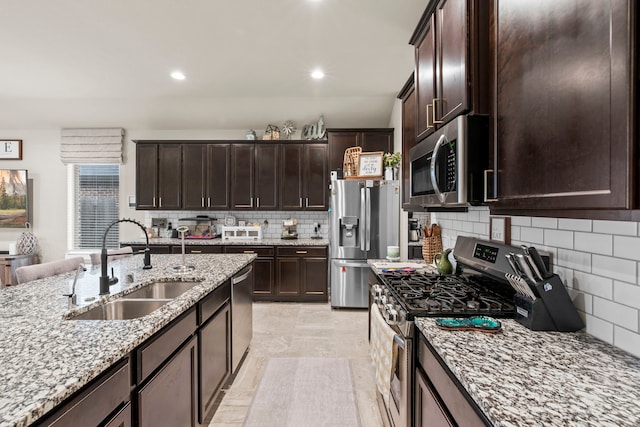 kitchen with recessed lighting, stainless steel appliances, a sink, light stone counters, and dark brown cabinets