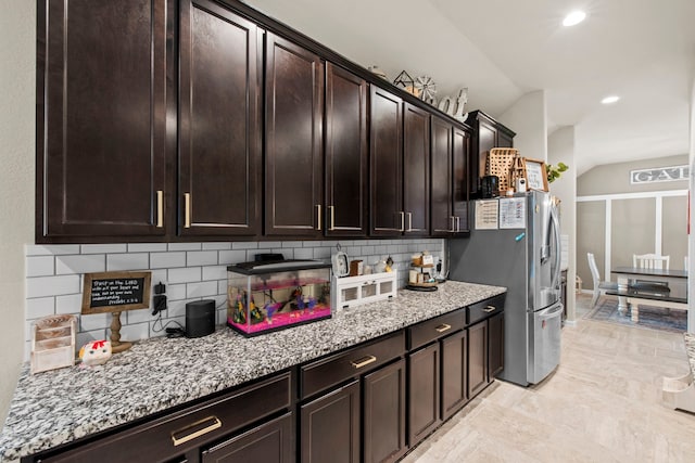kitchen featuring vaulted ceiling, dark brown cabinetry, light stone countertops, decorative backsplash, and recessed lighting