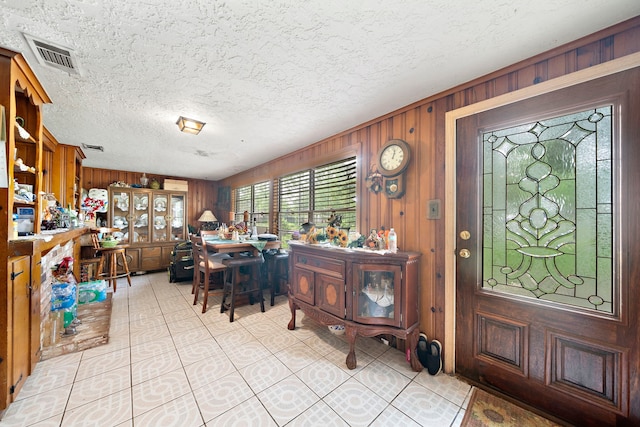 entryway with visible vents, light tile patterned floors, wooden walls, and a textured ceiling