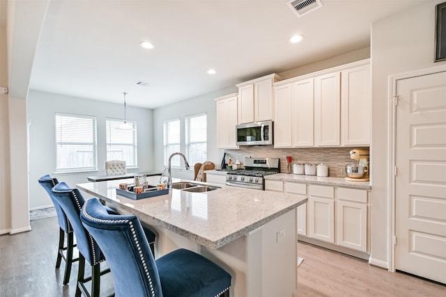 13710 Alaskan Brown Bear Trl, Crosby, TX 77532 - kitchen featuring a kitchen island with sink, appliances with stainless steel finishes, backsplash, light wood finished floors, and visible vents