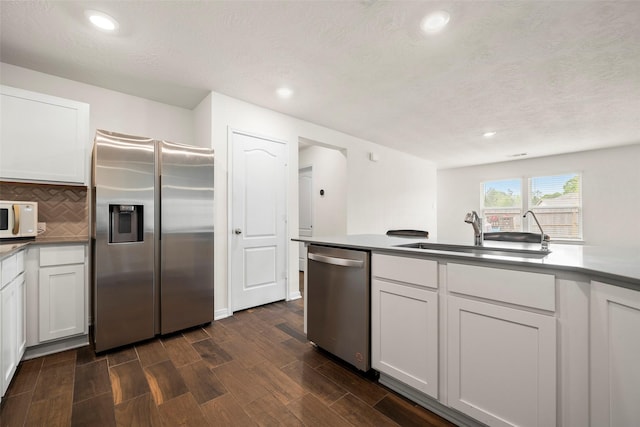kitchen with tasteful backsplash, dark wood-type flooring, a sink, white cabinets, and appliances with stainless steel finishes