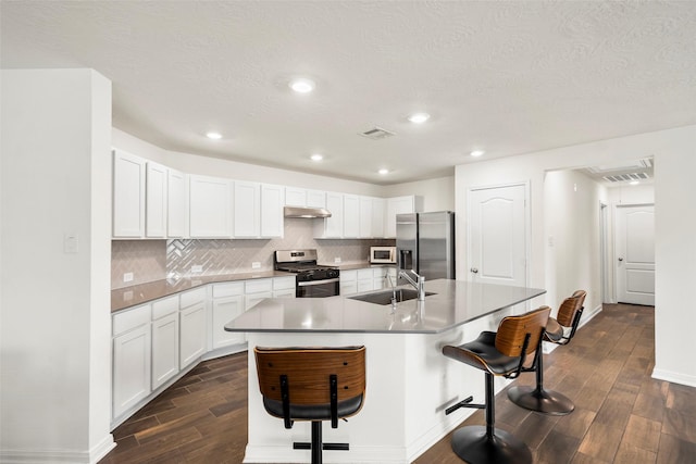 kitchen featuring a sink, a kitchen bar, dark wood finished floors, under cabinet range hood, and stainless steel appliances