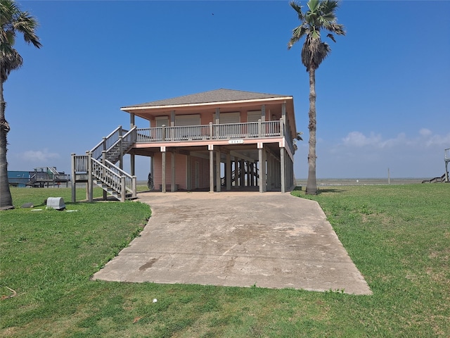 back of house with stairs, covered porch, concrete driveway, a carport, and a lawn