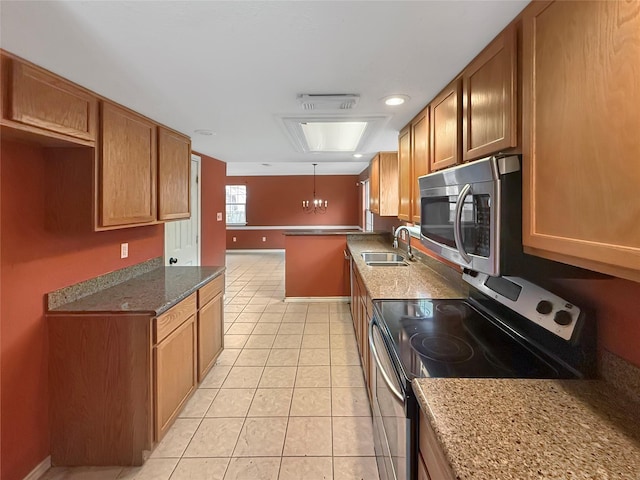 kitchen with light tile patterned flooring, brown cabinets, appliances with stainless steel finishes, dark stone countertops, and a sink
