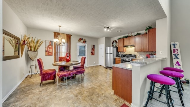 2201 Moonstone Ct, Texas City, TX 77591 - kitchen with stainless steel appliances, brown cabinets, under cabinet range hood, a chandelier, and light countertops