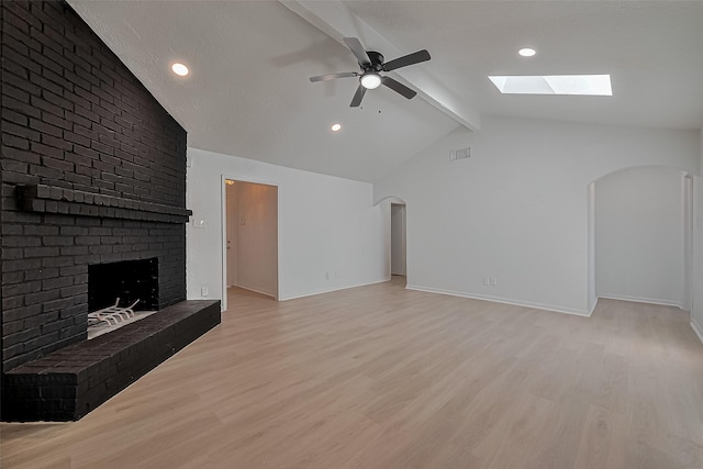 6219 Canada Dr, Pasadena, TX 77505 - unfurnished living room with arched walkways, vaulted ceiling with skylight, visible vents, a brick fireplace, and ceiling fan