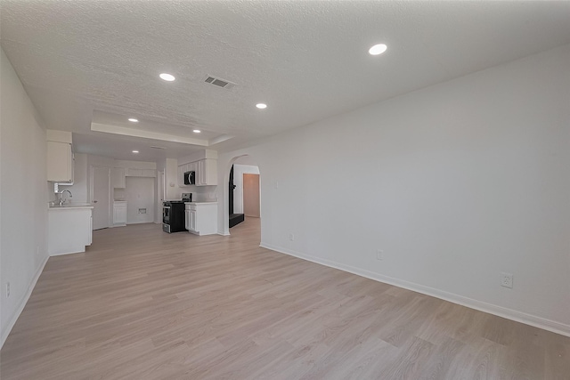 6219 Canada Dr, Pasadena, TX 77505 - unfurnished living room featuring a textured ceiling, a sink, arched walkways, visible vents, and light wood-style flooring