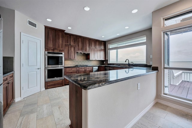 kitchen with dark stone counters, decorative backsplash, visible vents, stainless steel appliances, and a peninsula