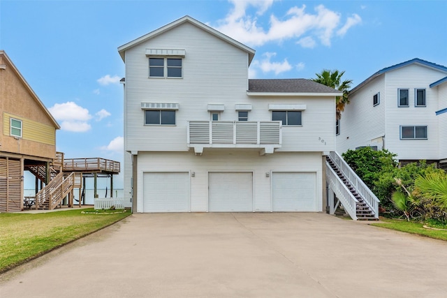 rear view of property featuring concrete driveway, a shingled roof, an attached garage, and stairs