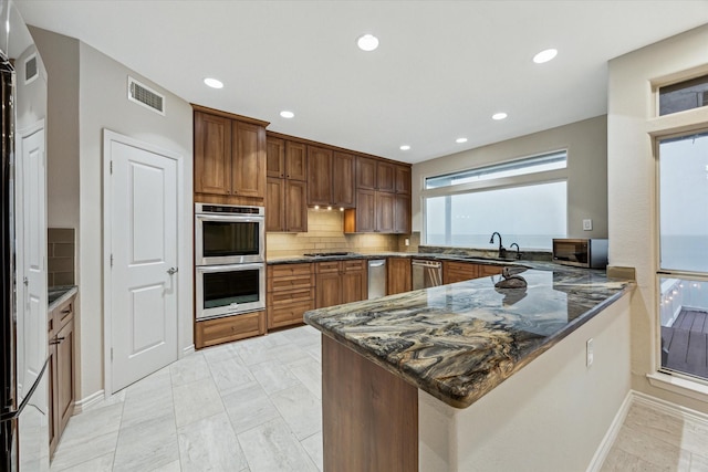 301 Isles End Rd, Tiki Island, TX 77554 - kitchen with stainless steel appliances, a peninsula, dark stone countertops, decorative backsplash, and baseboards