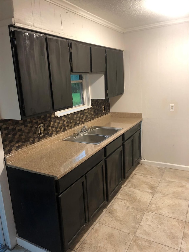 kitchen with a textured ceiling, light countertops, ornamental molding, a sink, and backsplash