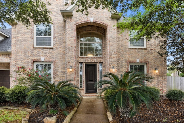 view of exterior entry with brick siding, fence, and a garage