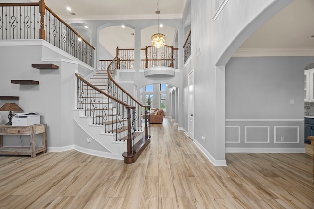 foyer featuring a towering ceiling, crown molding, arched walkways, stairway, and a notable chandelier