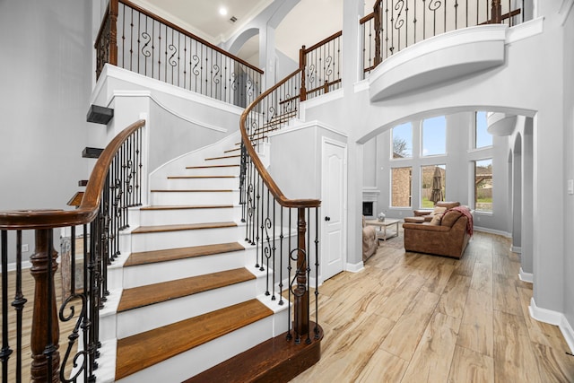 stairway with baseboards, a towering ceiling, wood finished floors, and a fireplace