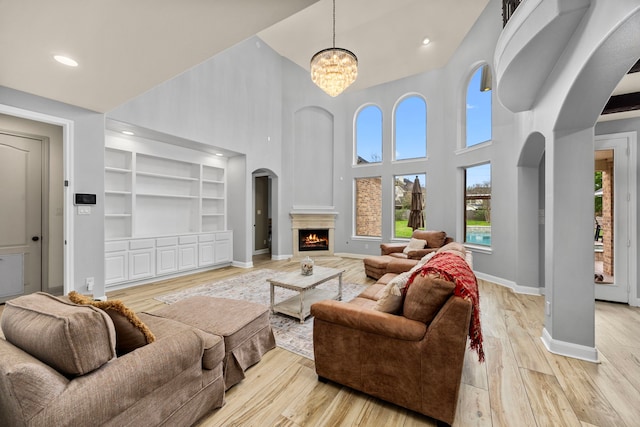 living area with a lit fireplace, arched walkways, baseboards, light wood finished floors, and a high ceiling