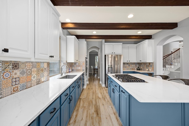 kitchen featuring blue cabinets, arched walkways, beam ceiling, a sink, and stainless steel appliances