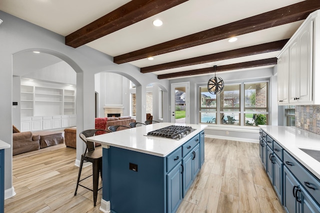 kitchen with white cabinets, stainless steel gas cooktop, arched walkways, blue cabinetry, and open floor plan