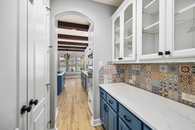 bar with arched walkways, tasteful backsplash, beamed ceiling, light wood finished floors, and oven