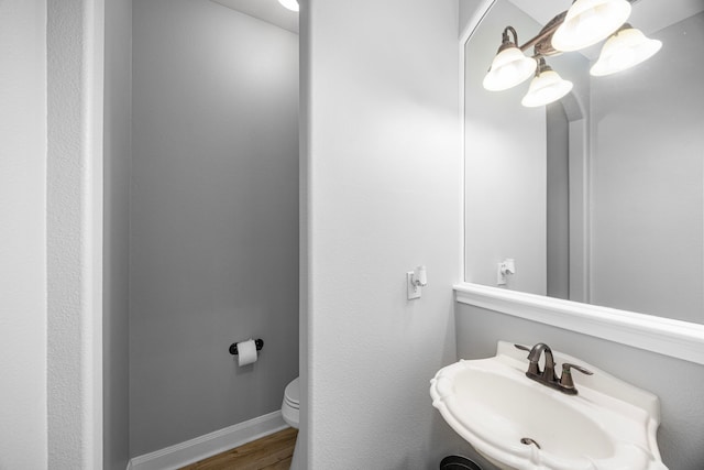 half bathroom featuring a sink, baseboards, toilet, and wood finished floors