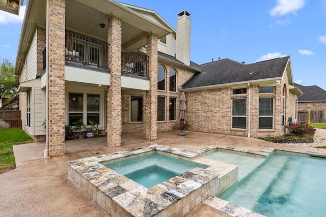 back of property featuring an in ground hot tub, a chimney, brick siding, a balcony, and a patio