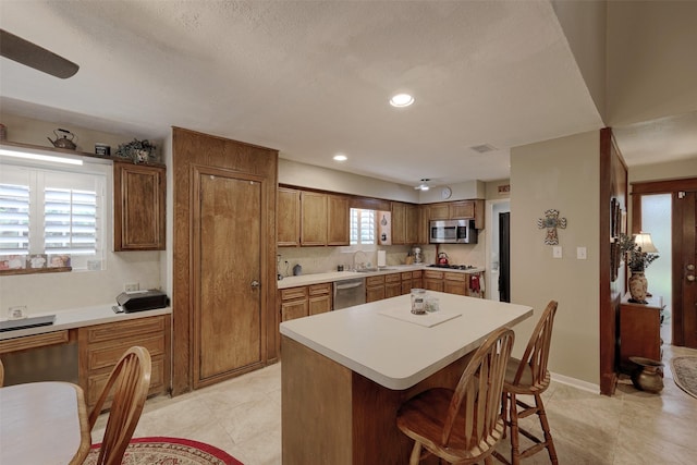 900 Manchester Dr, Conroe, TX 77304 - kitchen featuring stainless steel appliances, a sink, a breakfast bar, brown cabinetry, and light countertops