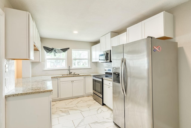 kitchen featuring stainless steel appliances, a sink, light marble finish flooring, light stone counters, and white cabinetry
