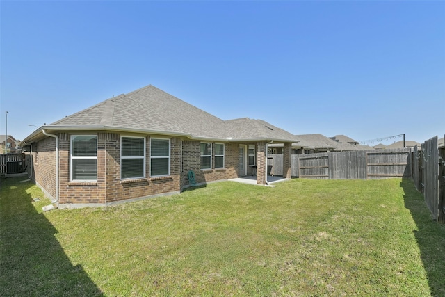 back of house featuring roof with shingles, a lawn, a fenced backyard, brick siding, and a patio area