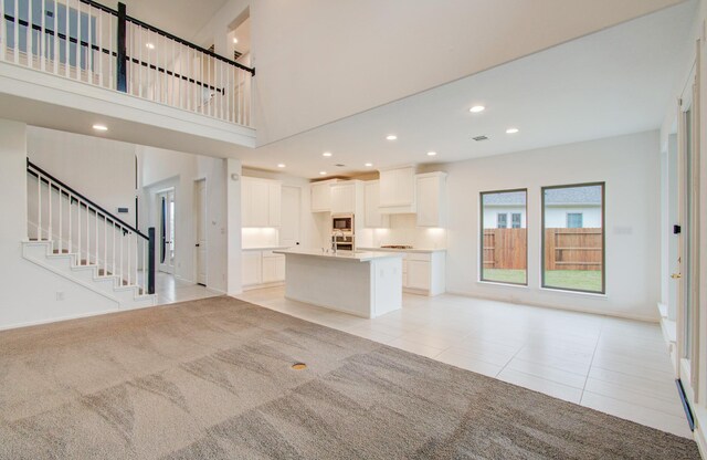 693 Cape Capri Dr, Katy, TX 77493 - unfurnished living room with light tile patterned flooring, stairway, recessed lighting, light carpet, and a high ceiling