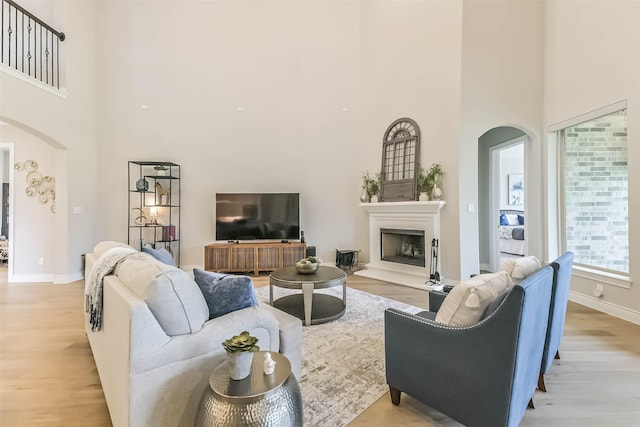 17429 Orchid Falls Ln, Conroe, TX 77302 - living area featuring arched walkways, a towering ceiling, light wood-style floors, and a fireplace with raised hearth