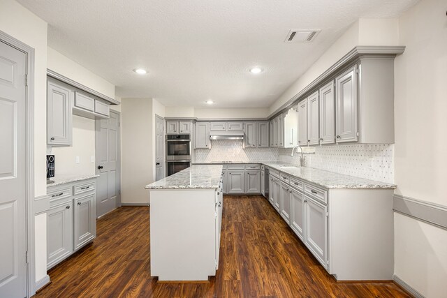 11814 Drexelbrook Dr, Houston, TX 77077 - kitchen with gray cabinetry, appliances with stainless steel finishes, a center island, dark wood finished floors, and under cabinet range hood