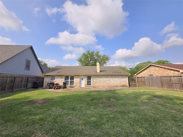rear view of house featuring a fenced backyard, brick siding, a yard, and a chimney