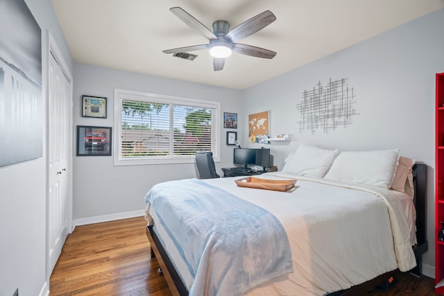 bedroom with visible vents, a closet, wood finished floors, baseboards, and a ceiling fan